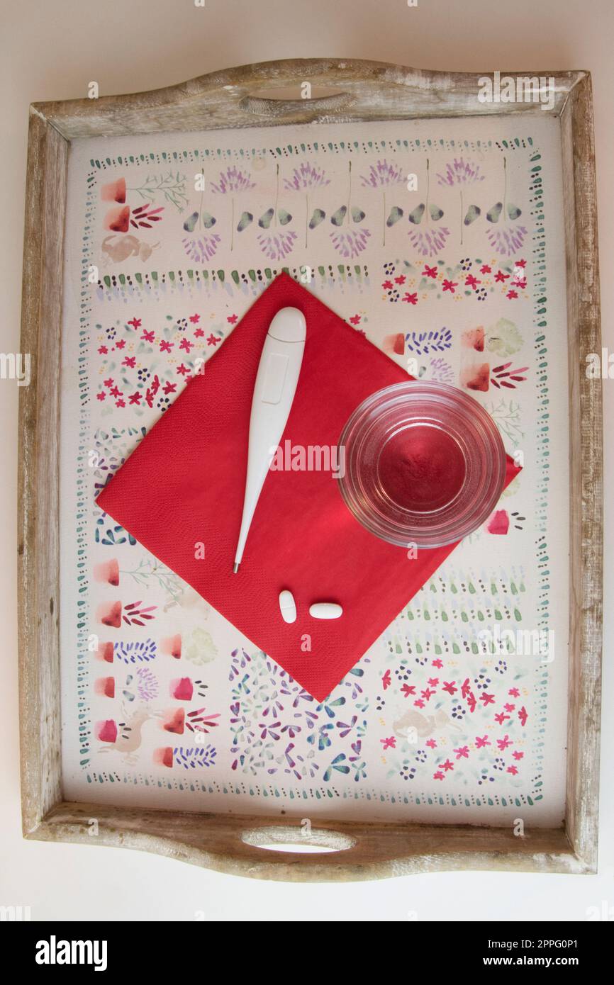 Tablett mit Wasserglas, Pillen und Thermometer, rot-weiß Stockfoto