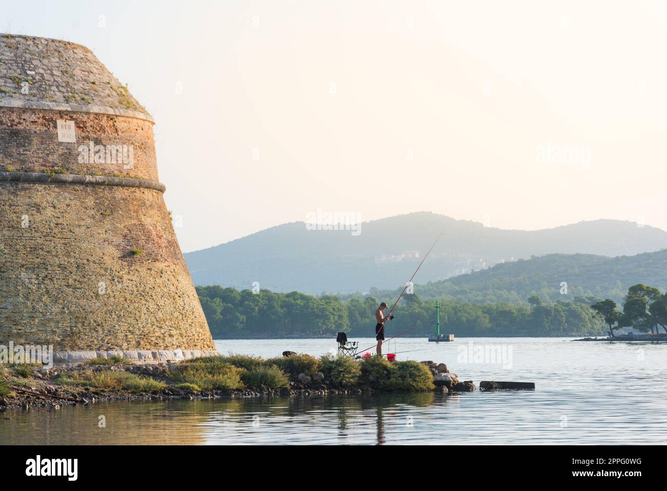 Der junge Mann sitzt und angelt auf dem Kanal sveti Ante in sibenik kroatien Stockfoto