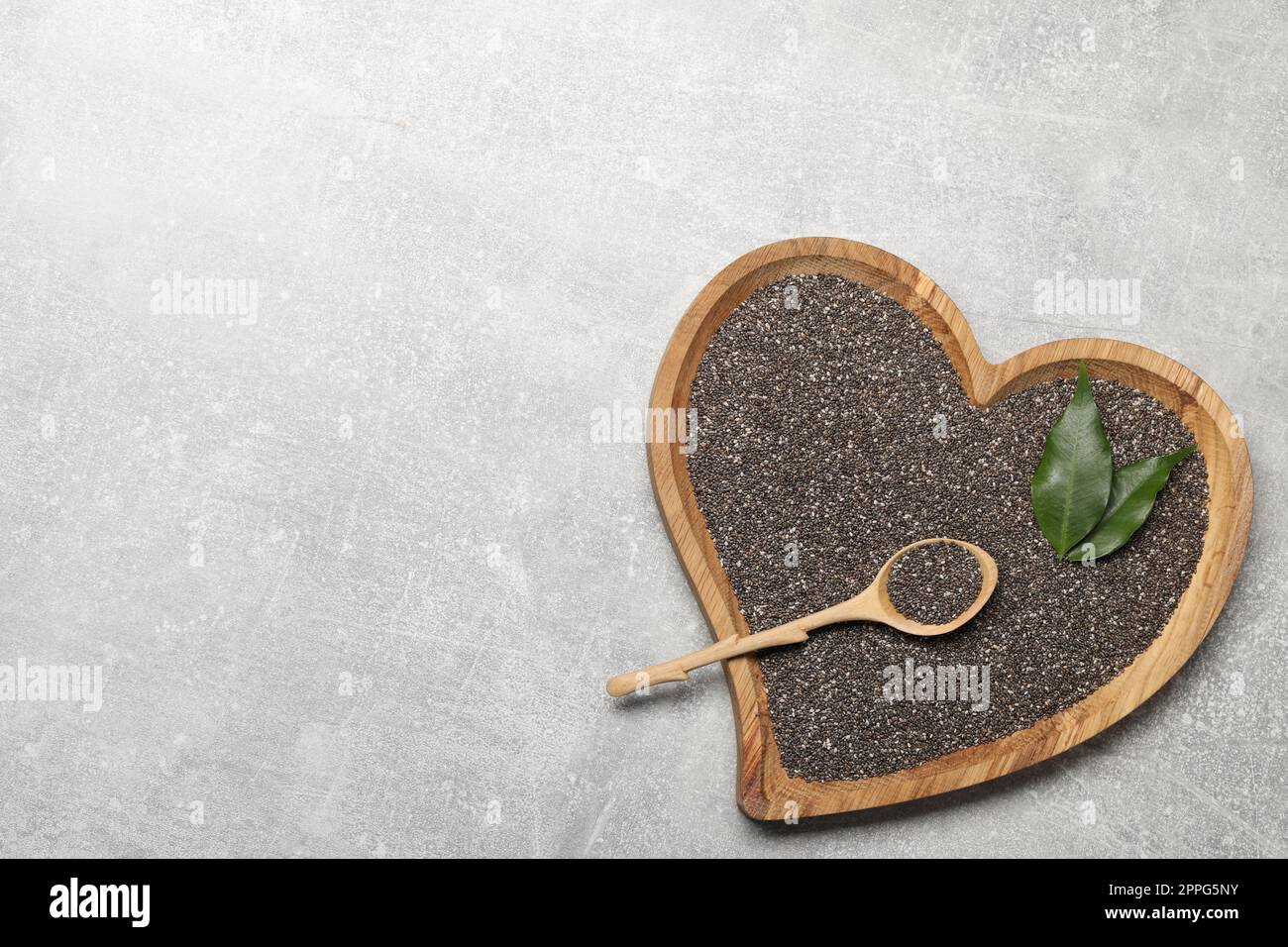 Chiasamen in Schüssel mit Löffel und grünen Blättern auf hellgrauem Tisch, Draufsicht. Platz für Text Stockfoto