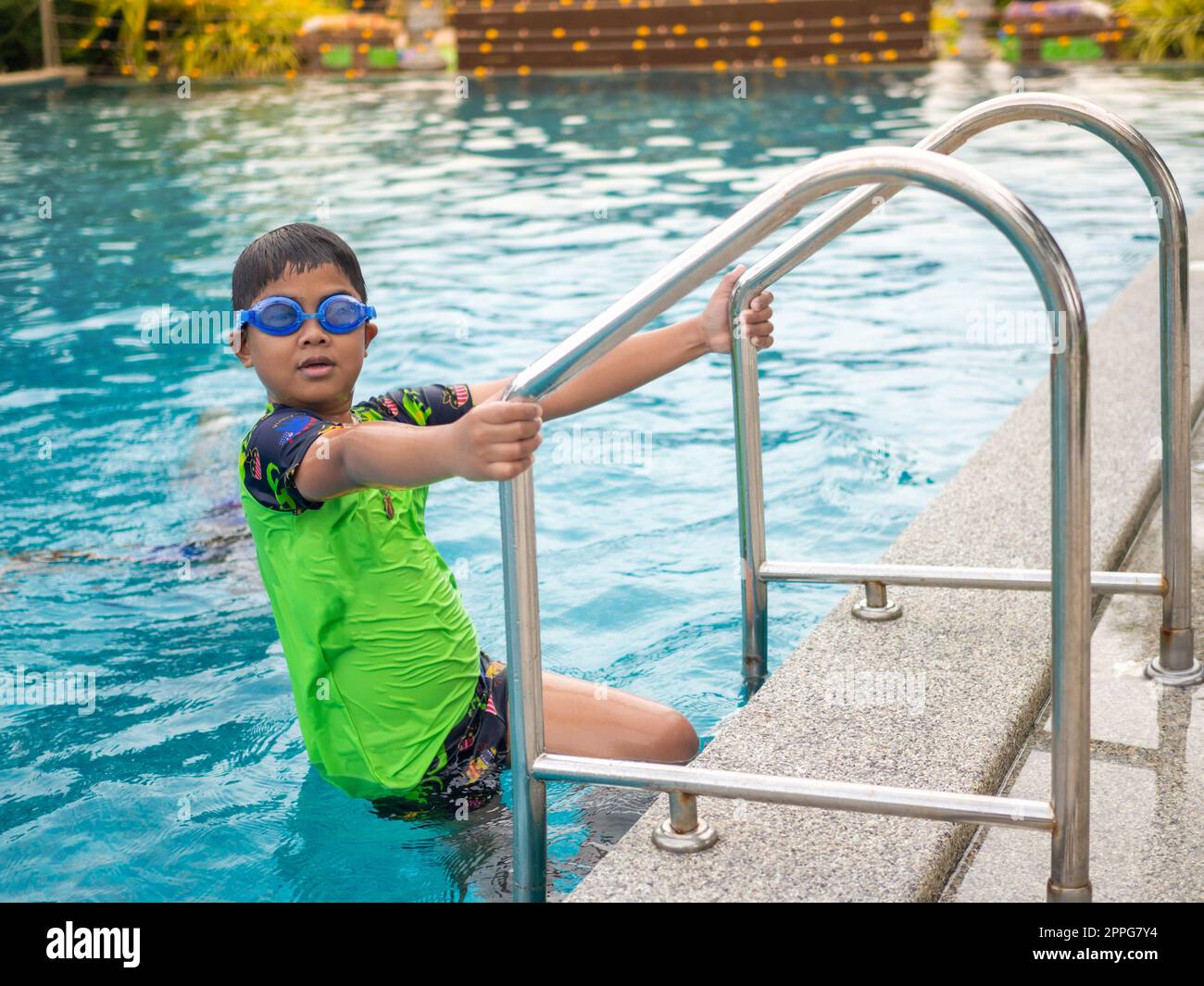Der Junge trägt eine Schwimmbrille auf einem blauen grünen Schwimmanzug mit Schwimmleiter Stockfoto