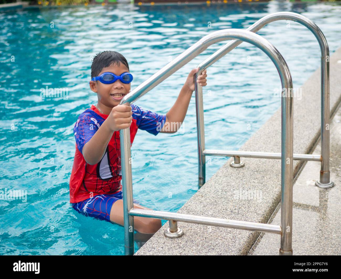 Der Junge trägt eine Schwimmbrille auf einem blauen roten Badeanzug mit Schwimmleiter Stockfoto