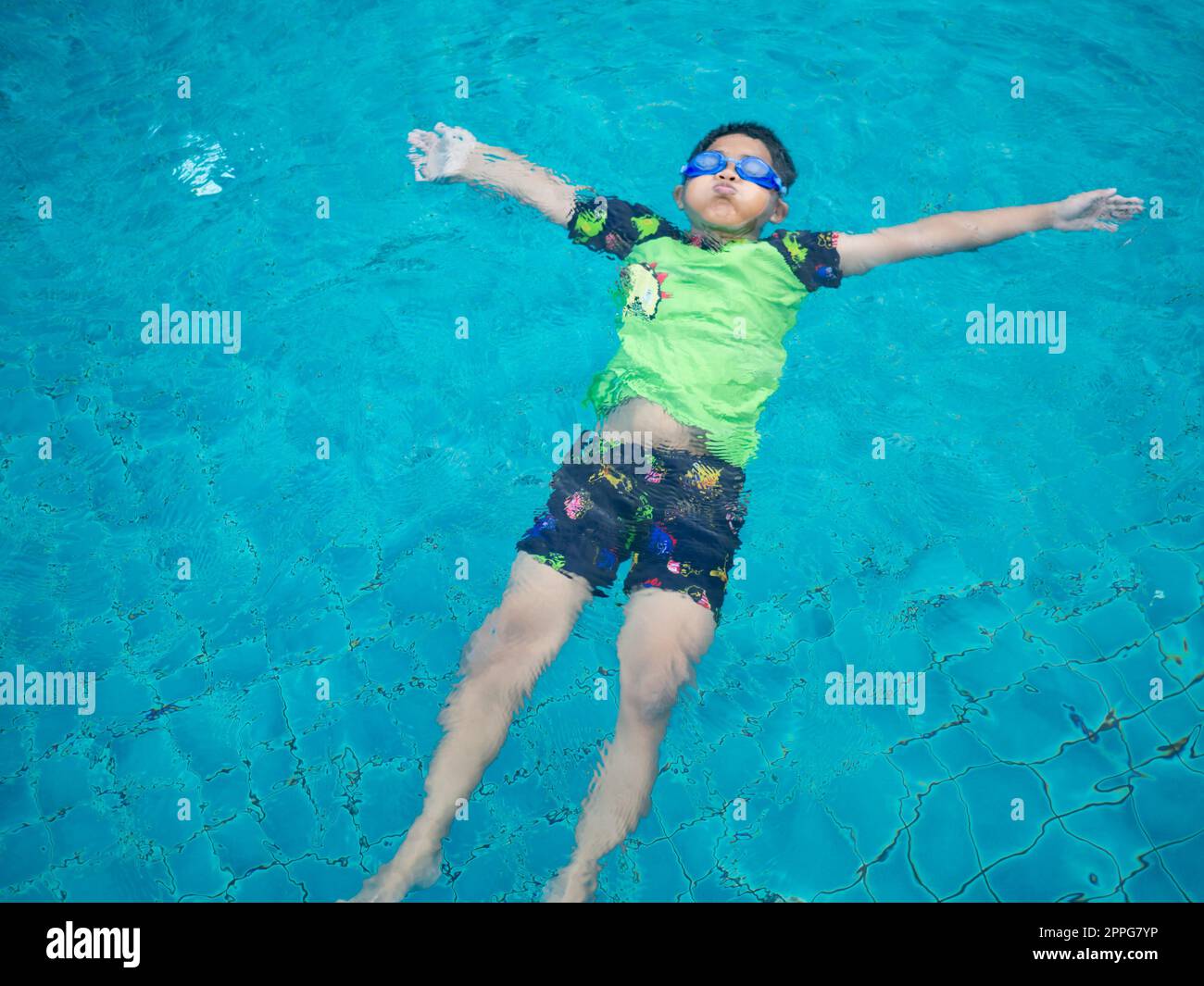 Junge mit Badeanzug und Brille, der in der Mitte des Pools mit blauem Wasserhintergrund schwimmend ist Stockfoto