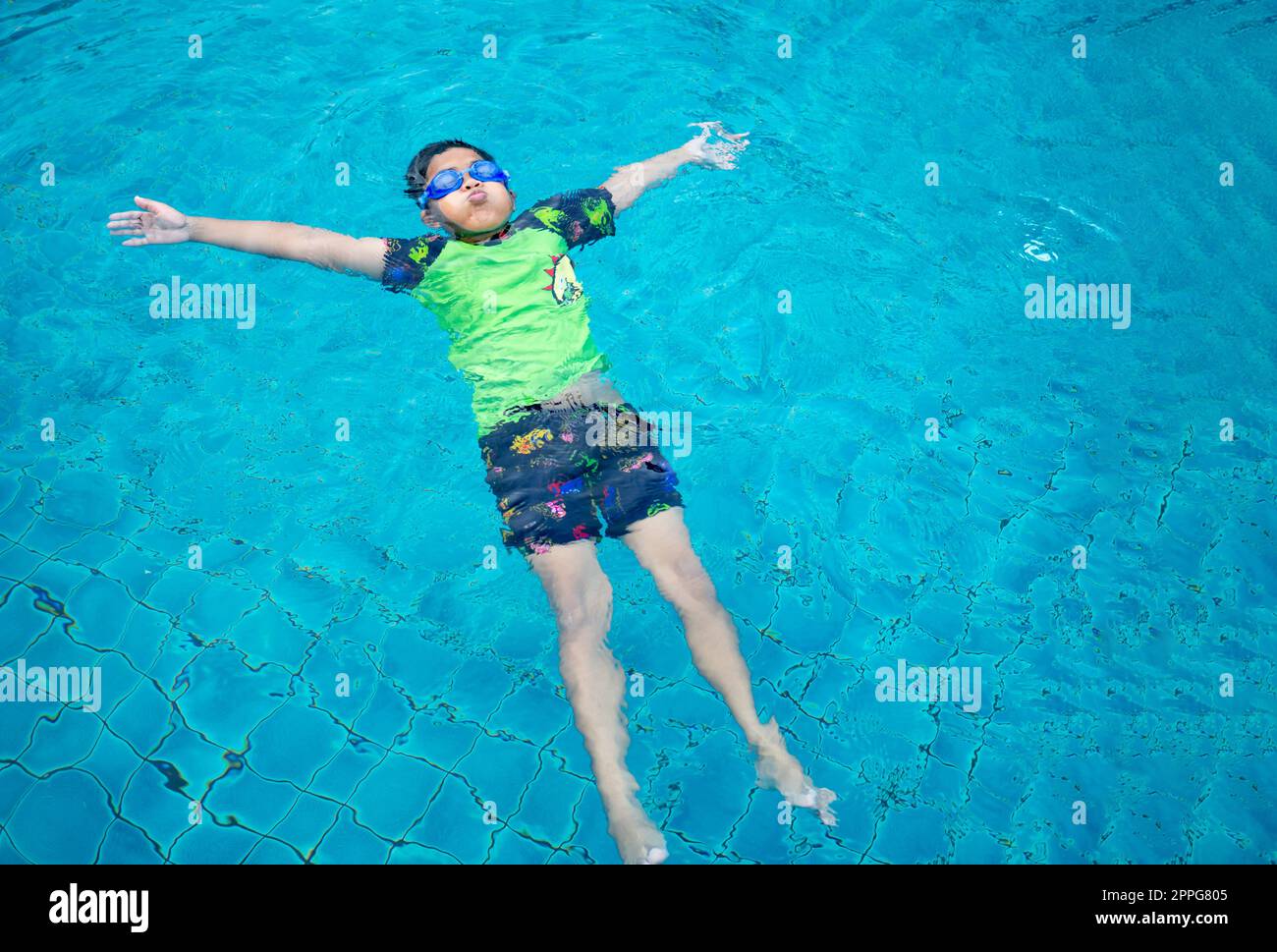 Junge mit Badeanzug und Brille, der in der Mitte des Pools mit blauem Wasserhintergrund schwimmend ist Stockfoto
