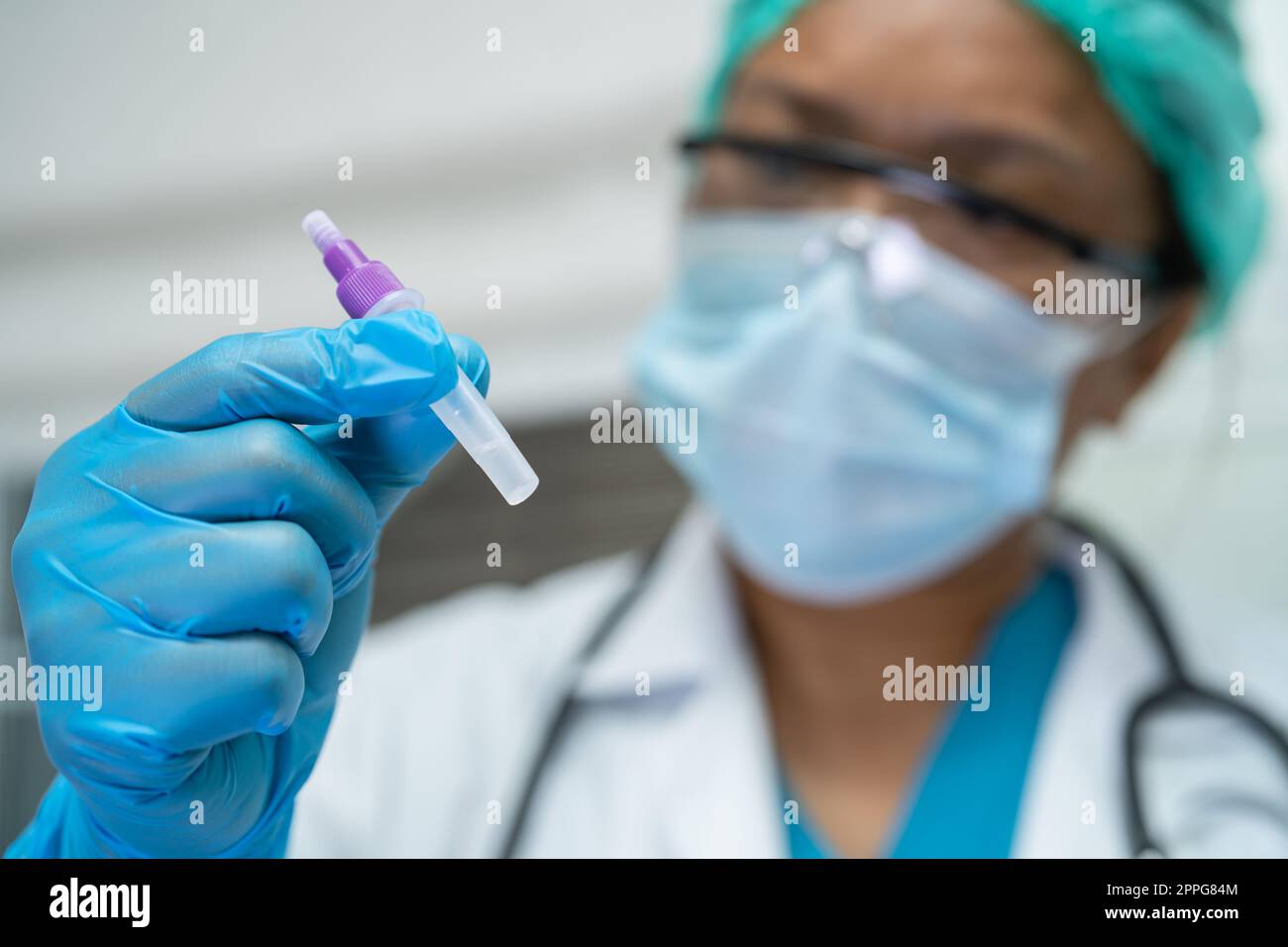 Ein asiatischer Arzt im PSA-Anzug zeigt ein positives Testergebnis mit dem Speichelantigen-Testkit zur Kontrolle des Covid19-Coronavirus im Krankenhaus. Stockfoto