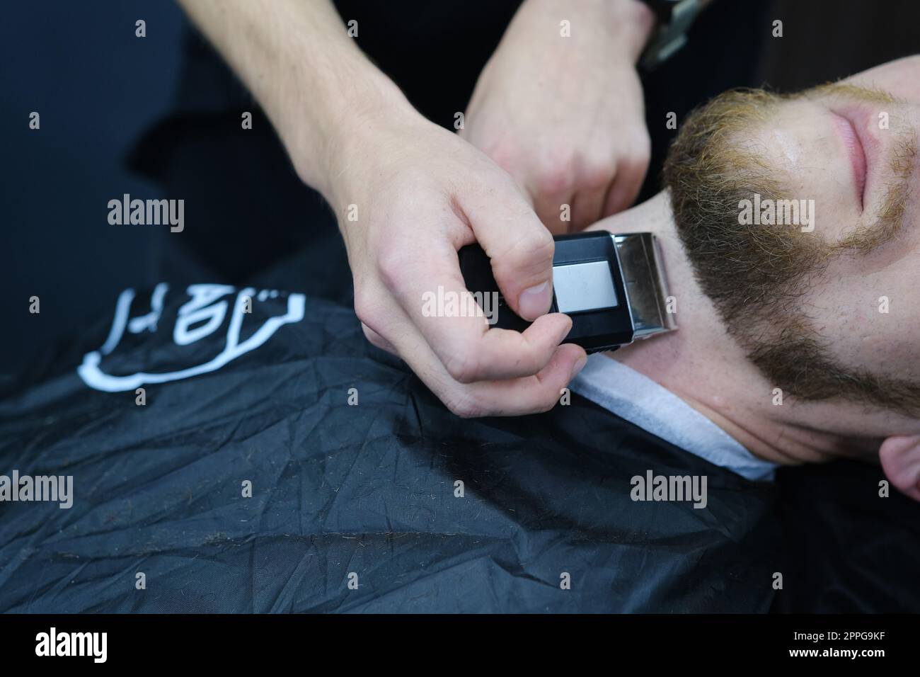 Professioneller Friseur rasiert den Bart des Kunden mit einem elektrischen Trimmer. Haarschnitt vom Bart eines Mannes in einem Friseursalon. Friseurmänner. Werbe- und Friseurgeschäft-Konzept Stockfoto