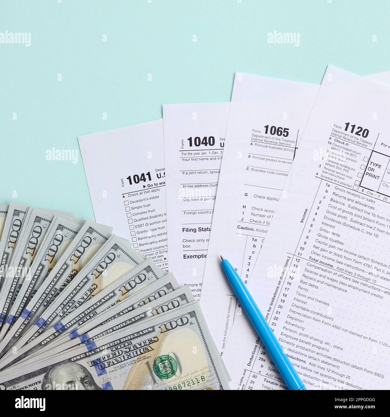 Die Steuerformulare liegen fast 100-Dollar-Scheine und ein blauer Stift auf hellblauem Hintergrund. Einkommensteuererklärung Stockfoto