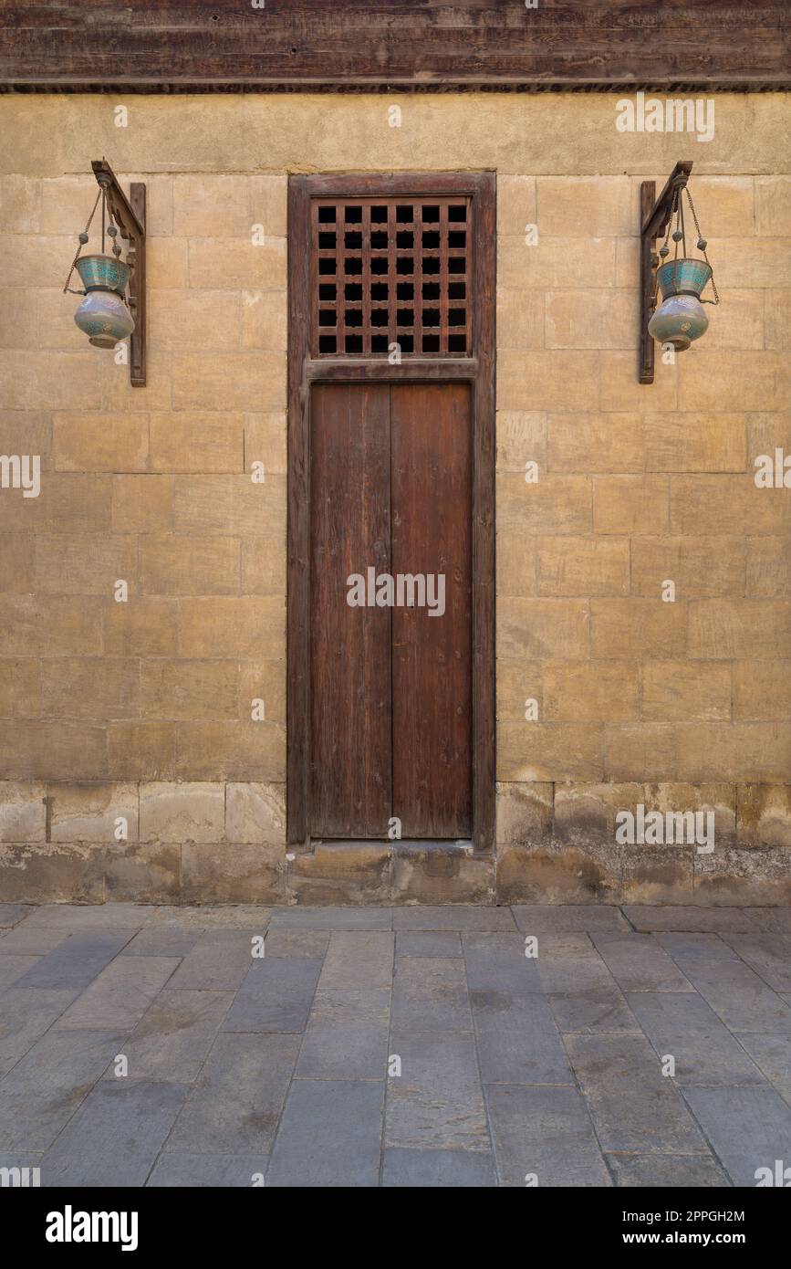Geschlossene Holztür und Straßenlaternen aus arabischem Glas hängen an einer Holzstange in alten Steinmauern Stockfoto
