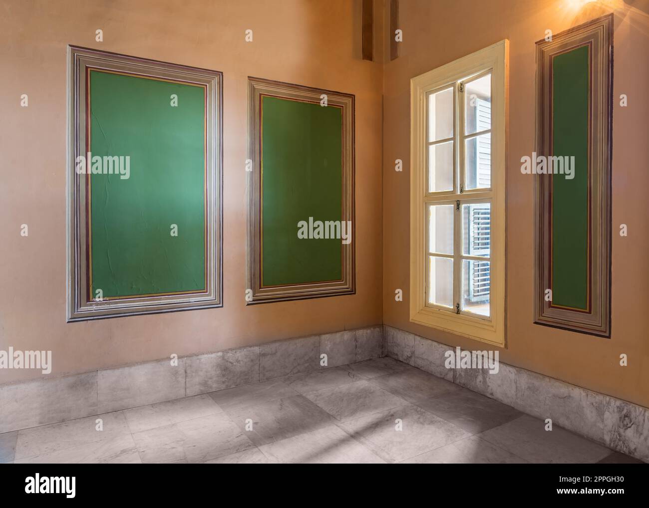 Drei grüne Rahmen mit kunstvoll verziertem Rand und Fenster mit grünem Rollladen an orangefarbenen Wänden mit Marmorboden Stockfoto