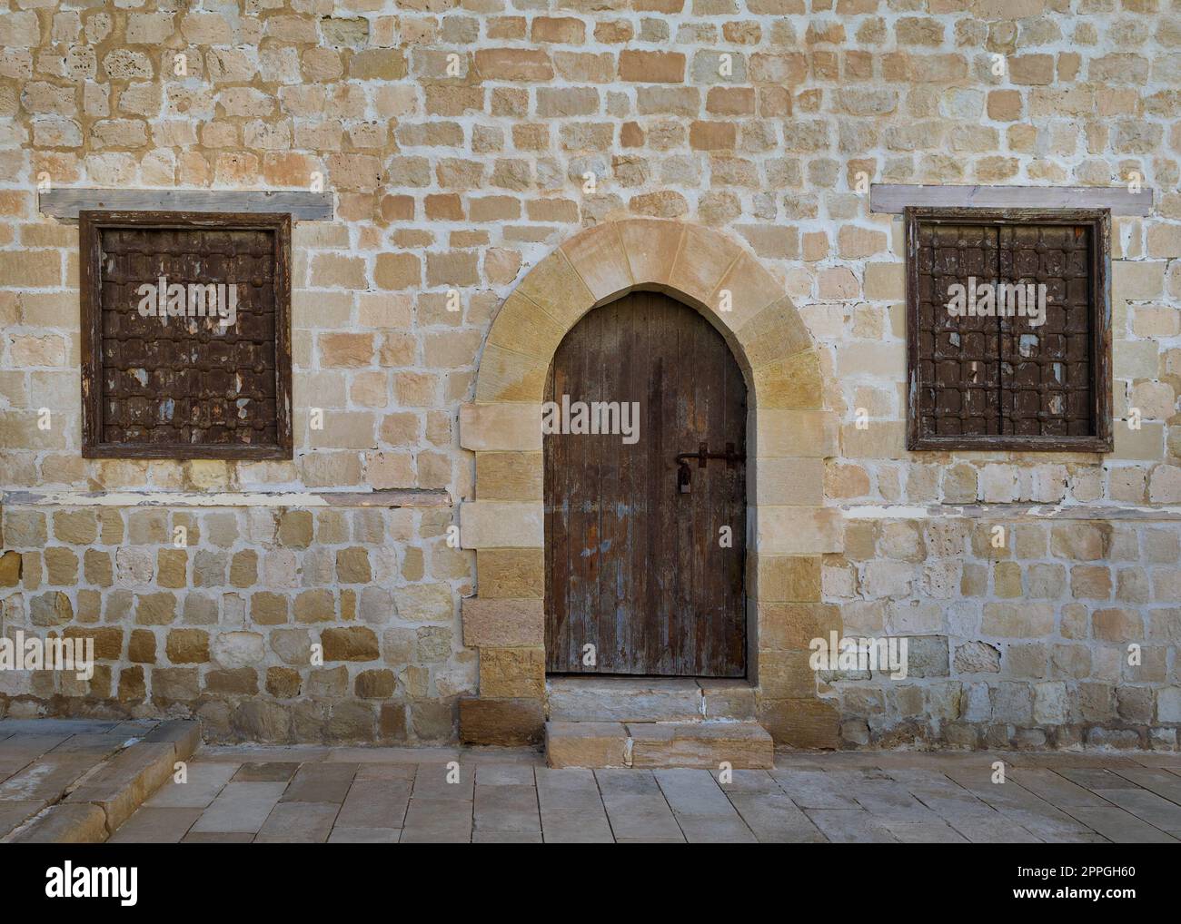 Alte verwitterte Bogenholztüren und zwei geschlossene rostige schmiedeeiserne Fenster an Steinmauern Stockfoto