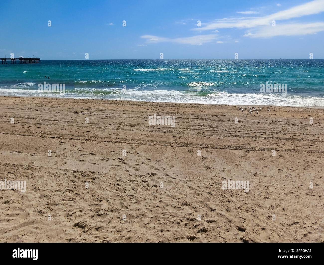 Fernblick auf die sonnige und tropische blaue Wasserküste mit Menschen, Vegetation, Booten und Gebäuden im Hintergrund von über dem Wasser aus gesehen. Stockfoto