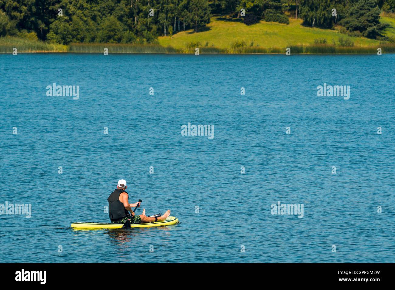 Seitenansicht foto eines Mannes, der auf dem Sup-Board schwimmt und sich entspannt Stockfoto