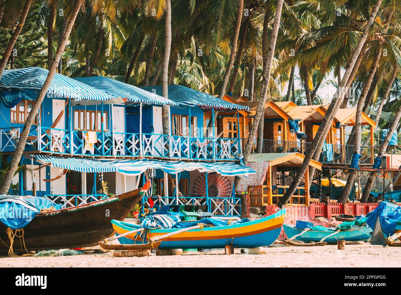 Canacona, Goa, Indien. Fischerboot Und Berühmte Gemalte Gästehäuser Am Palolem Strand Vor Dem Hintergrund Der Hohen Palmen In Sonnentag. Stockfoto