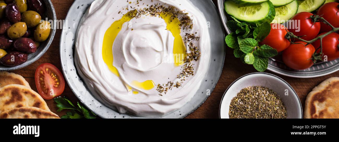 Lob Joghurt Frischkäse mit Olivenöl, Zaatar, Oliven, Gemüse und Pita Brot, Banner. Traditionelles arabisches, griechisches oder nahöstliches Frühstück mit Stockfoto