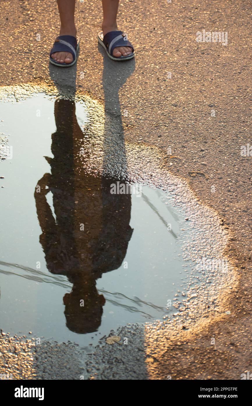 Silhouette eines Kindes auf einem kleinen Teich an der Straße Stockfoto