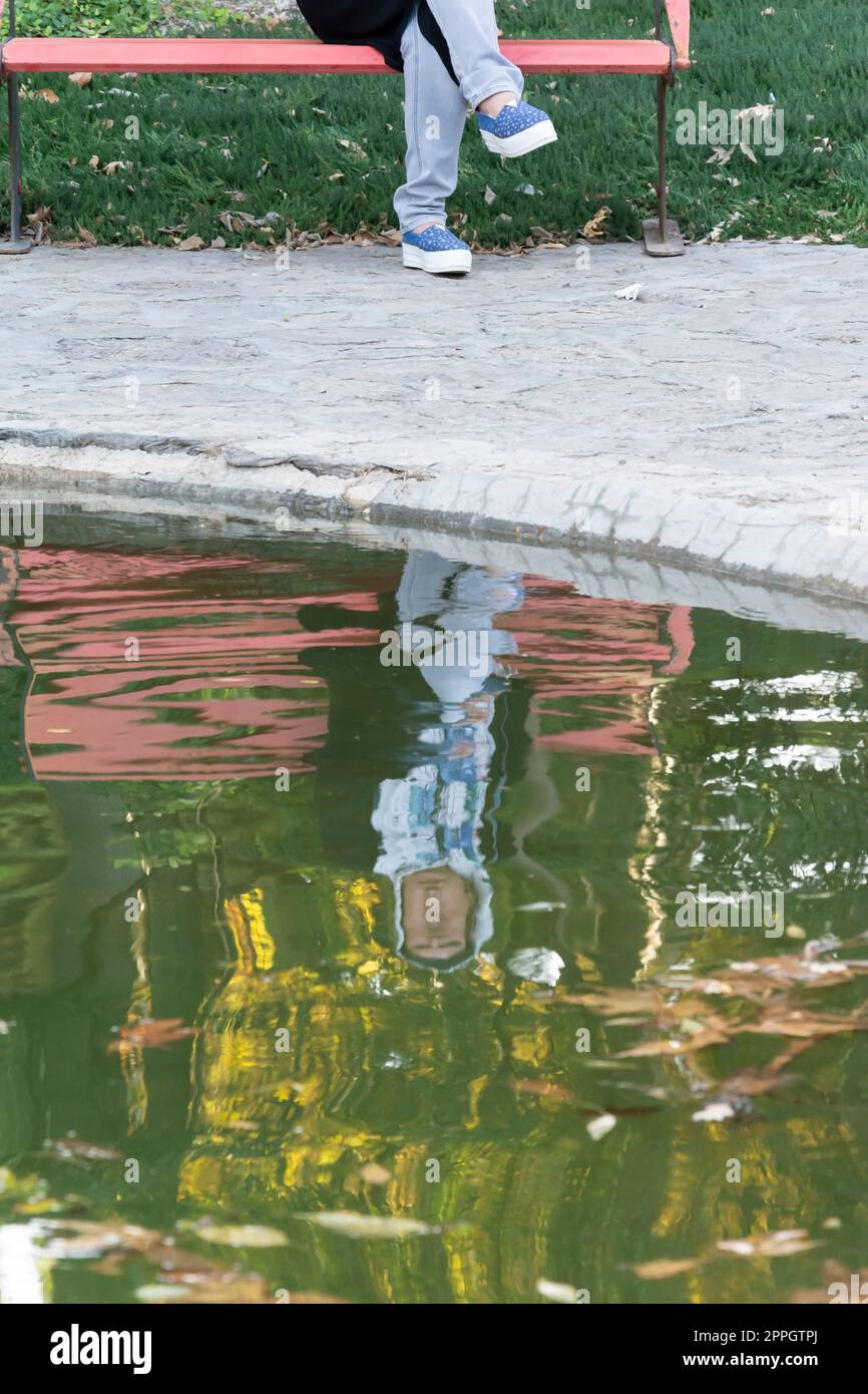 Junge Frau reflektiert über Wasserpfütze im Park Stockfoto