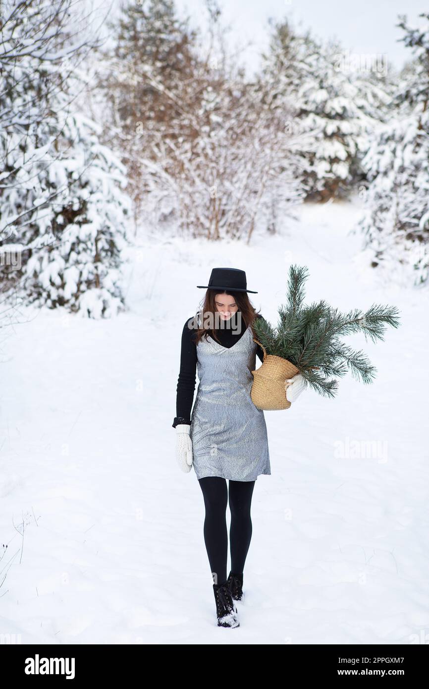 Ein junges Mädchen in silbernem Kleid und Hut steht mit dem Rücken inmitten eines wunderschönen Winterwaldes. Stockfoto