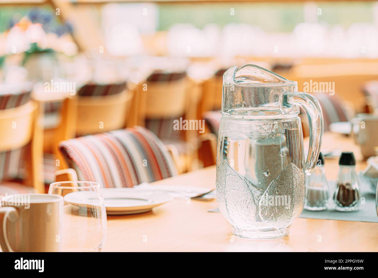 Gemütliches Interieur Des Summer Cafe. Krug Mit Eiskalt Kaltem Eiswasser Auf Dem Tisch Und Besteck Ausgelegt Stockfoto