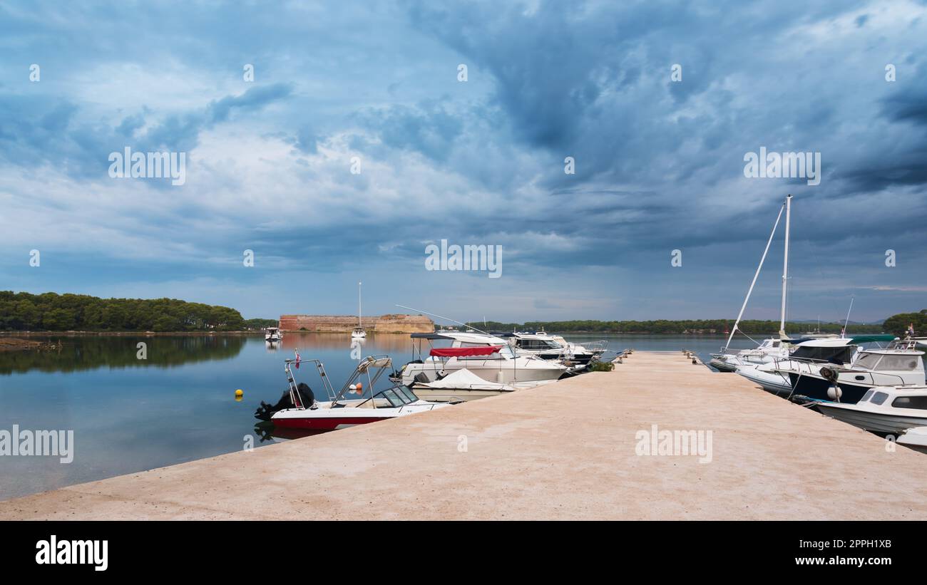 Pier mit Booten in der Bucht an den Festungen von sveti nikola mit dunklen Wolken, sibenik Stockfoto
