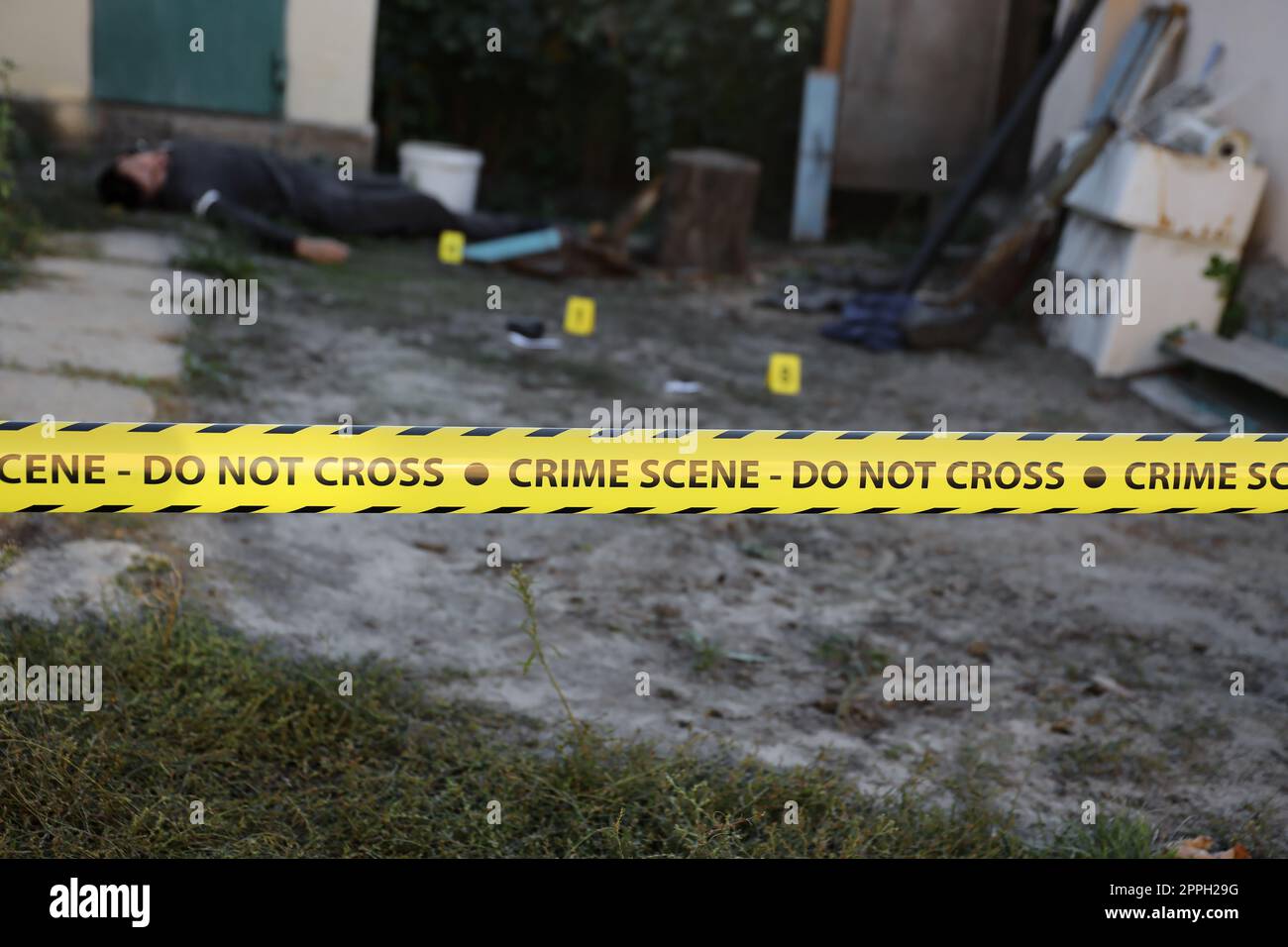 Opfer eines Gewaltverbrechens in einem Wohnheim am Abend. Leiche eines toten Mannes unter dem gelben Polizeiband und Beweismarkierungen am Tatort Stockfoto
