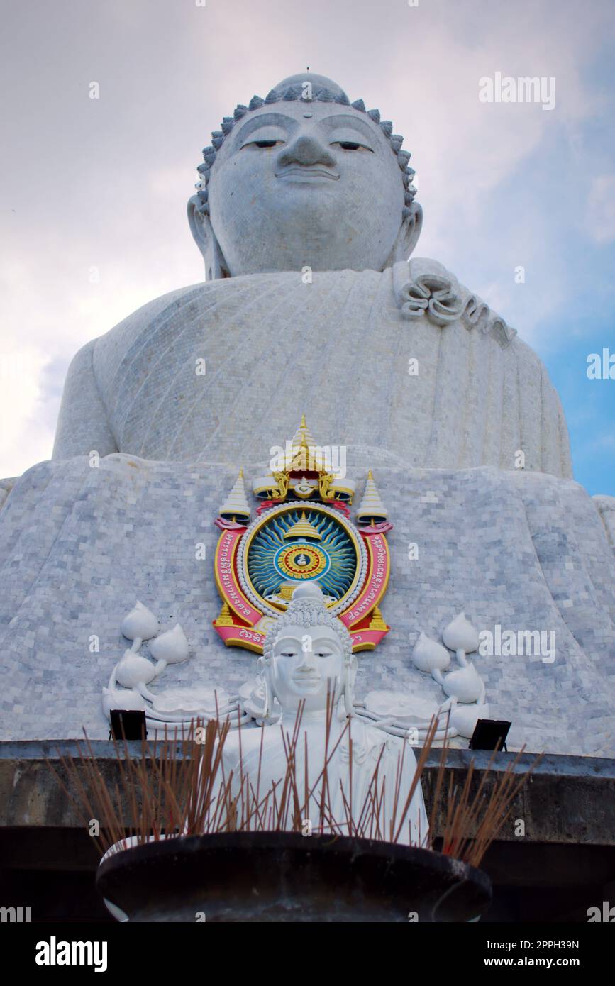 Riesige Marmor statue des Sitzenden Buddha in Phuket, Thailand, als "Big Buddha" bekannt. Eine kleinere Statue mit Weihrauch Angebote im Vordergrund. Stockfoto