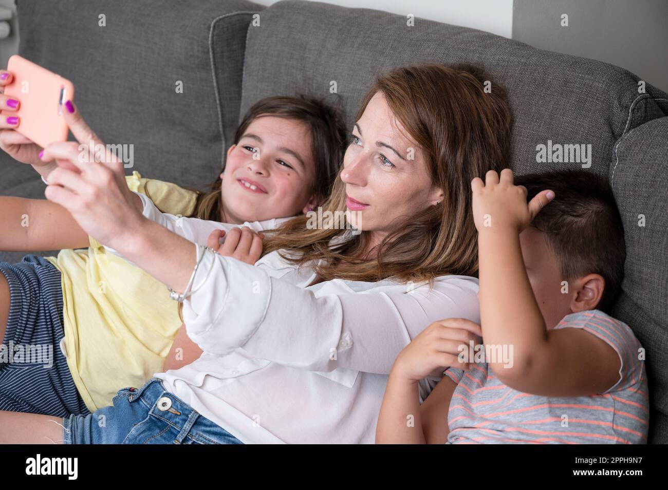 Glückliche Mutter mit ihren Kindern macht ein Selfie oder Videogespräch mit dem Vater oder Verwandten auf dem Sofa. Konzept von Technologie, neue Generation, Familie, Verbindung, Elternschaft. Stockfoto