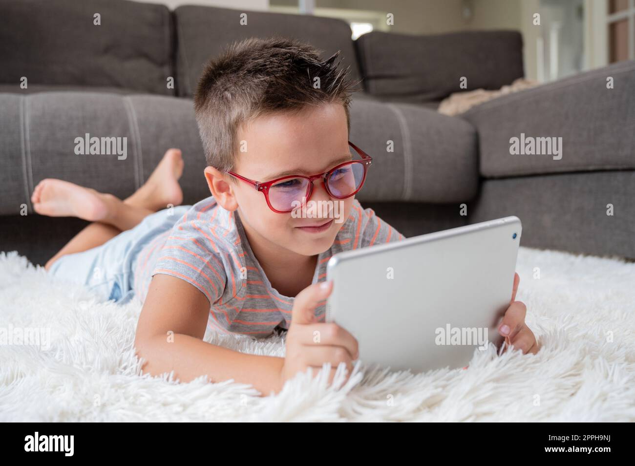 Ein niedlicher kleiner Junge, der zu Hause ein digitales Tablet auf dem Boden benutzt. Stockfoto