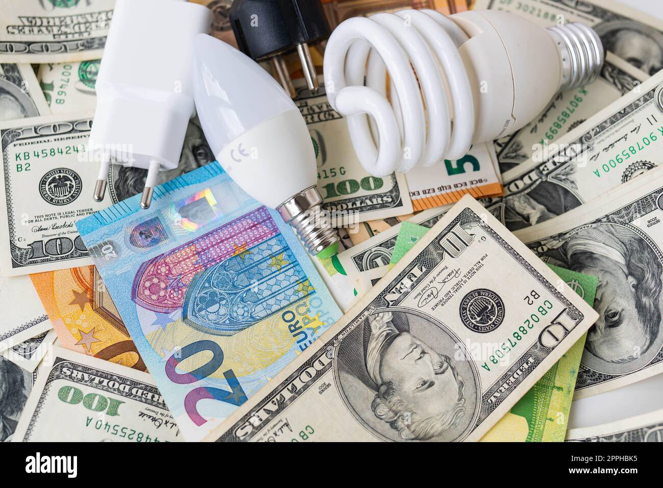 Das Konzept der Energiekrise, Preiserhöhungen. Euro- und Dollar-Banknoten, Münzen auf dem Hintergrund einer Lampe, Stecker, Schnur. Steuerzeit, Rechnungszahlung, Zählrechner. Stockfoto