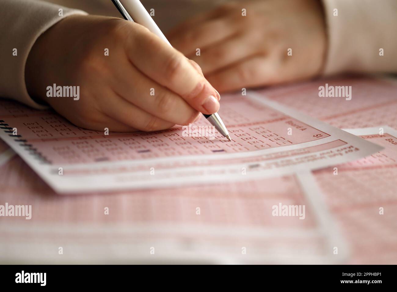 Ein Lotterielos ausfüllen. Eine junge Frau spielt im Lotto und träumt davon, den Jackpot zu gewinnen. Weibliche Handzeichen auf rotem Lotterielos Stockfoto