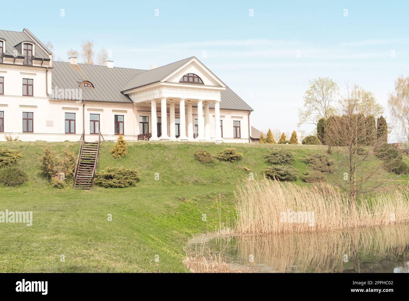 Weißrussland, Dorf Radzivilki, 01.05.22. Restauriertes altes Herrenhaus in Belarus. Blick auf den Haupteingang mit Säulen am Ufer des Teichs Stockfoto