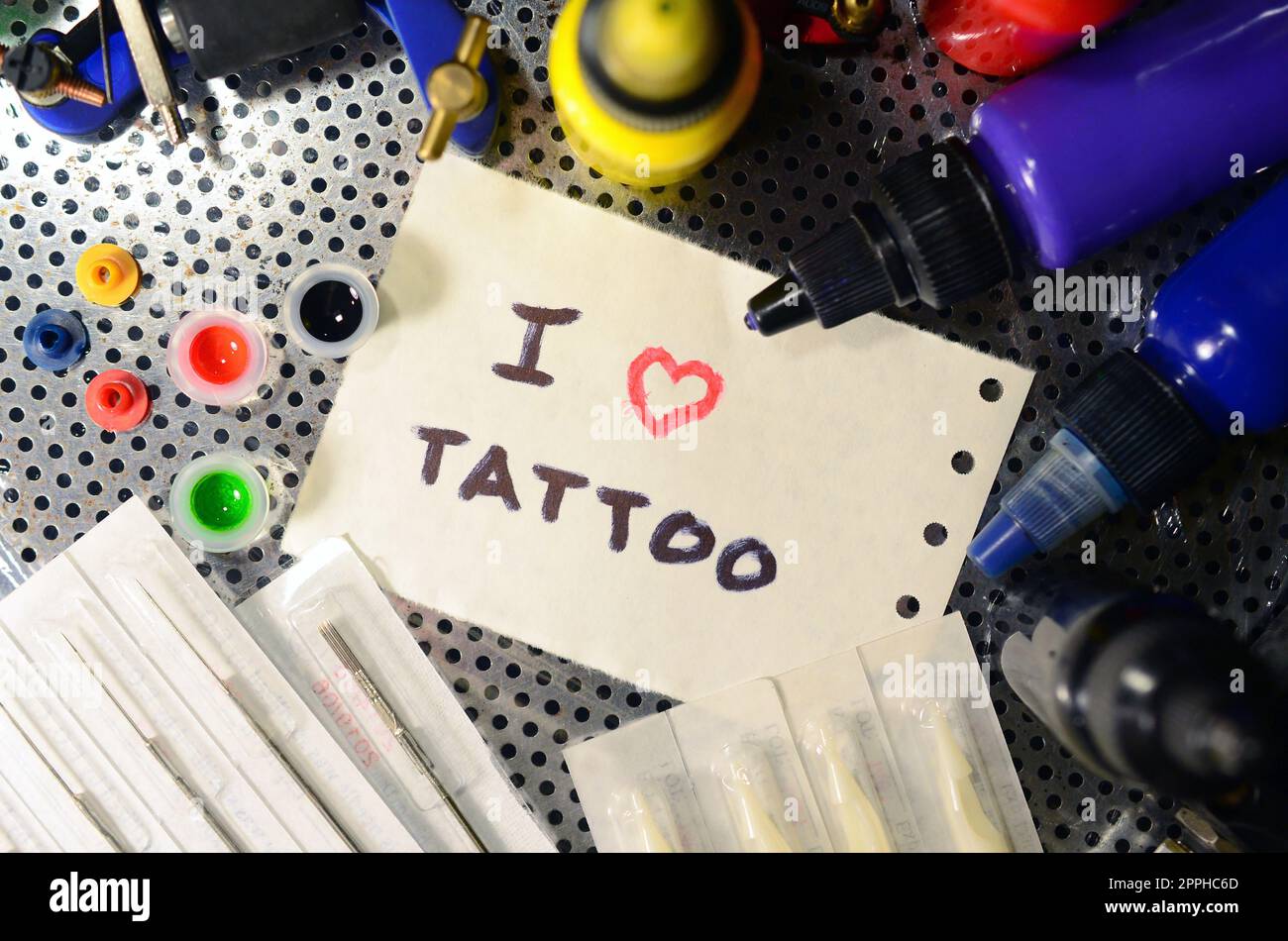 Ich liebe Tattoo. Der Text ist auf einem kleinen Blatt Papier unter verschiedenen Geräten zum Tätowieren geschrieben Stockfoto