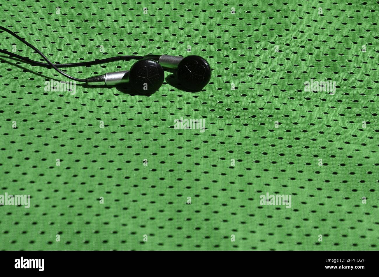 Schwarz Ohrhörer liegen auf der grünen Sportswear aus Polyester nylon Faser. Das Konzept der Musik beim Sport Training mit moderner Technologie Stockfoto