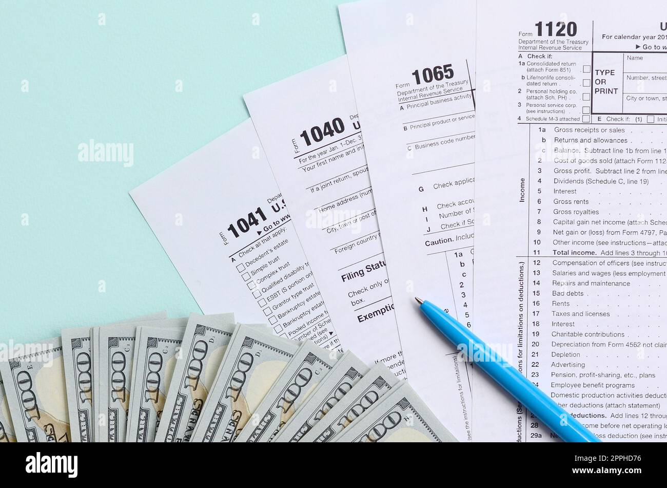 Die Steuerformulare liegen fast 100-Dollar-Scheine und ein blauer Stift auf hellblauem Hintergrund. Einkommensteuererklärung Stockfoto
