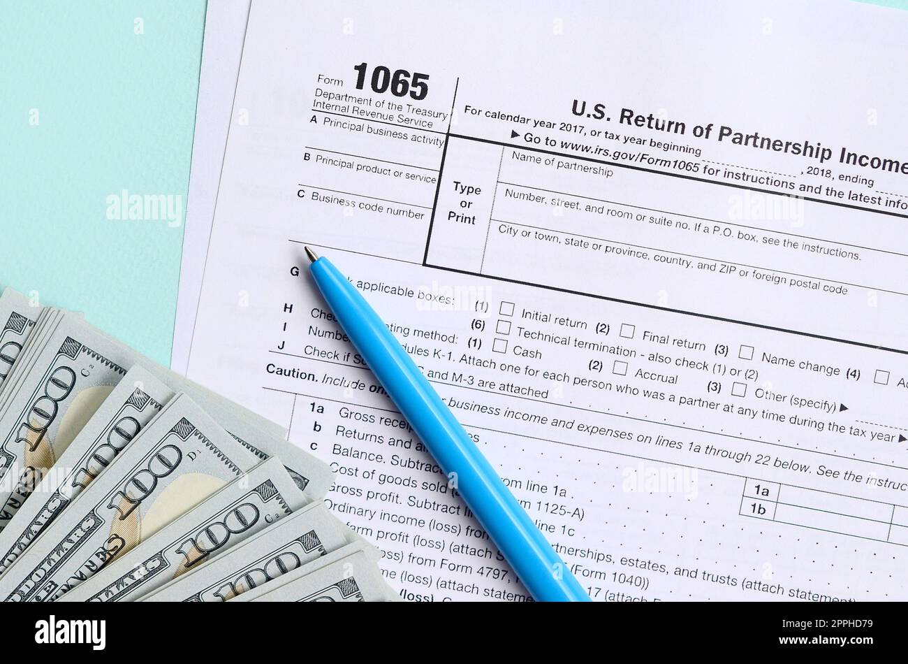 Das Steuerformular für 1065 liegt in etwa 100-Dollar-Scheinen und einem blauen Stift auf hellblauem Hintergrund. US Return for Parentship Income Stockfoto