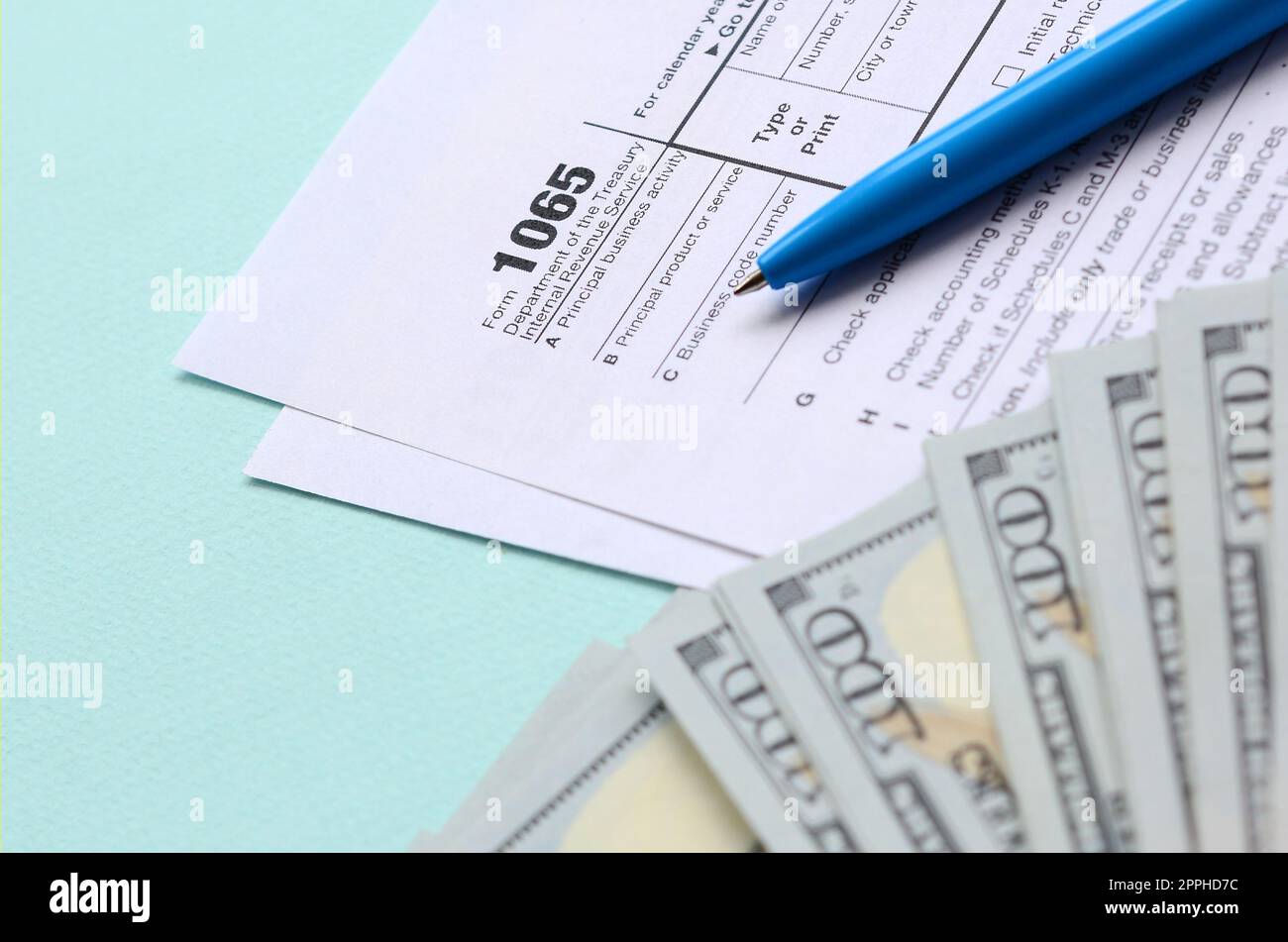 Das Steuerformular für 1065 liegt in etwa 100-Dollar-Scheinen und einem blauen Stift auf hellblauem Hintergrund. US Return for Parentship Income Stockfoto