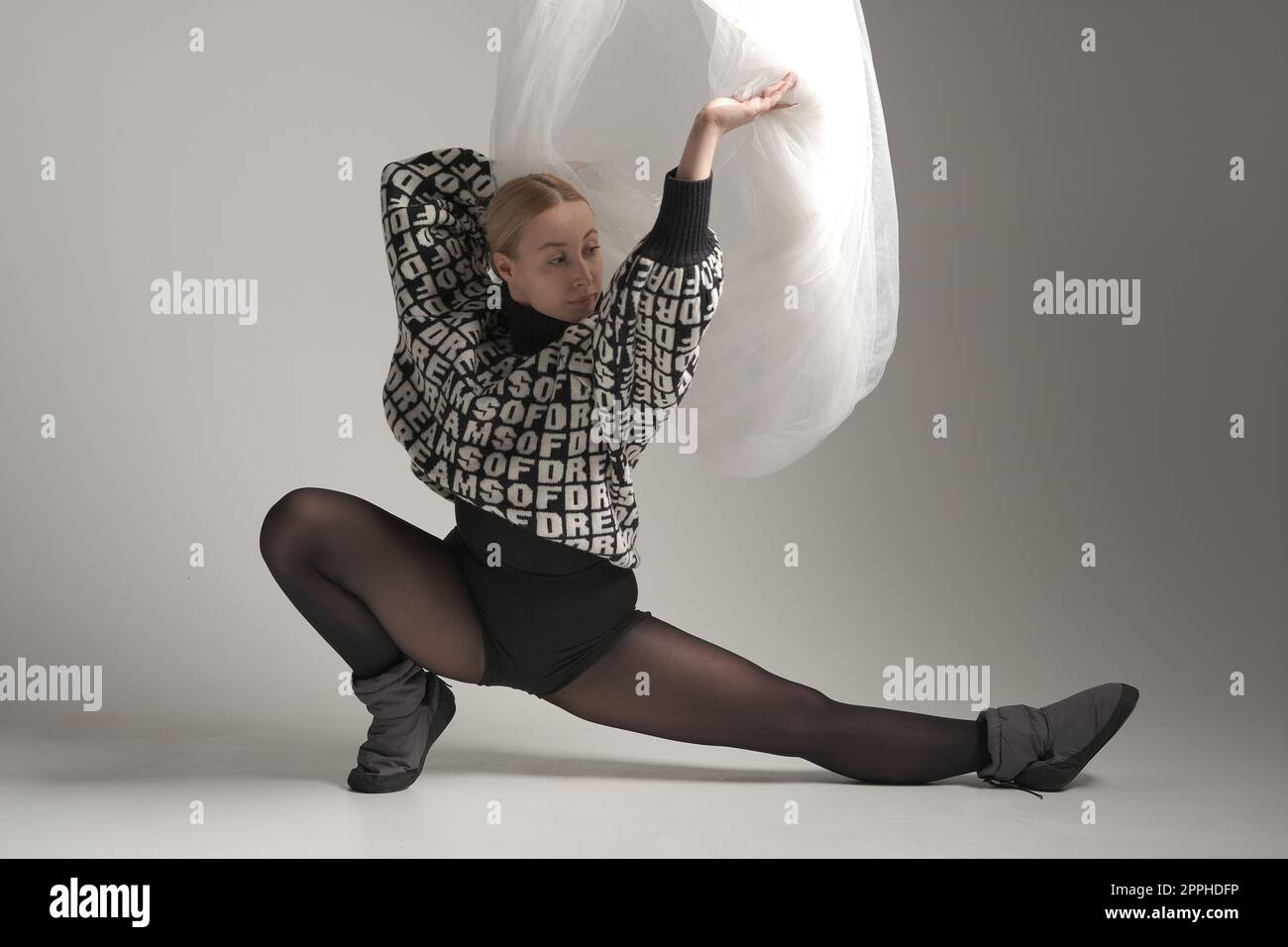 Ballerina mit Seidenstoff, moderne Balletttänzerin mit wellenförmigem weißem Stoff, grauer Hintergrund. Mit Text auf Pullover, VON dem DU TRÄUMST Stockfoto