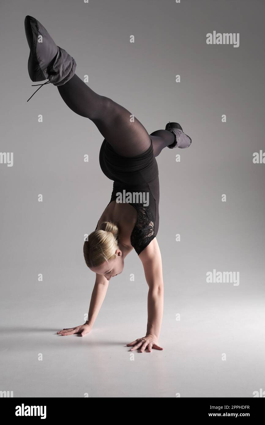 Balletttänzerin Frau schwarzes Kleid auf grauem Hintergrund, Ballerina posiert und zeigt ihre Flexibilität auf grauem Hintergrund im Studio Stockfoto