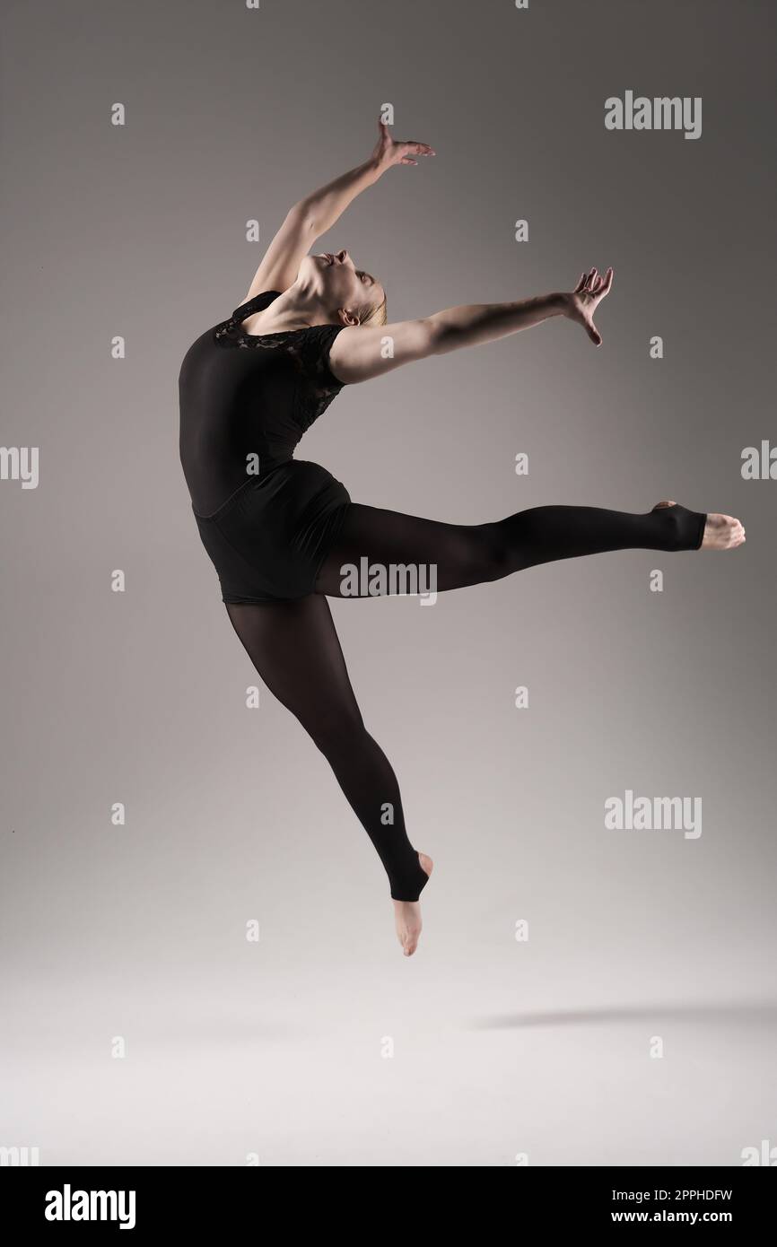 Balletttänzerin Frau schwarzes Kleid auf grauem Hintergrund, Ballerina posiert und zeigt ihre Flexibilität auf grauem Hintergrund im Studio Stockfoto