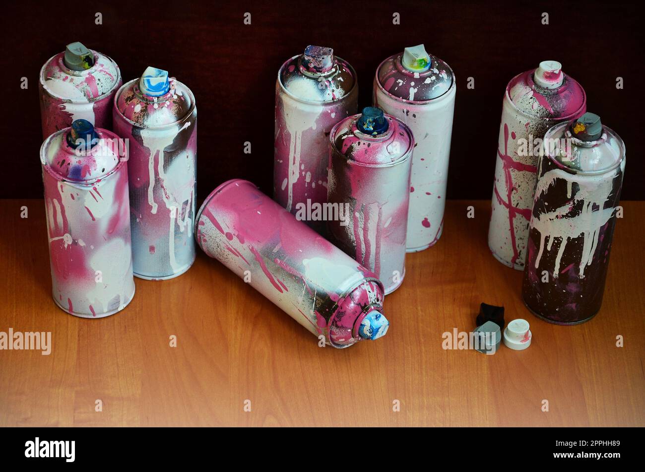 Stillleben mit einer großen Anzahl von gebrauchten bunten Spraydosen Aerosolfarbe, die auf der behandelten Holzoberfläche in der Graffiti-Werkstatt des Künstlers liegen. Schmutzige und verschmutzte Dosen für Sprühkunst Stockfoto