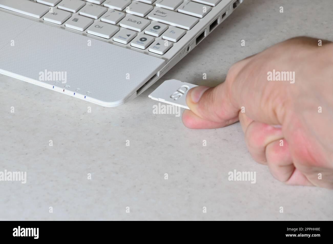 Eine männliche Hand steckt eine weiße kompakte SD-Karte in den entsprechenden Eingang an der Seite des weißen Netbooks. Der Mensch nutzt moderne Technologien, um Speicher und digitale Daten zu speichern Stockfoto