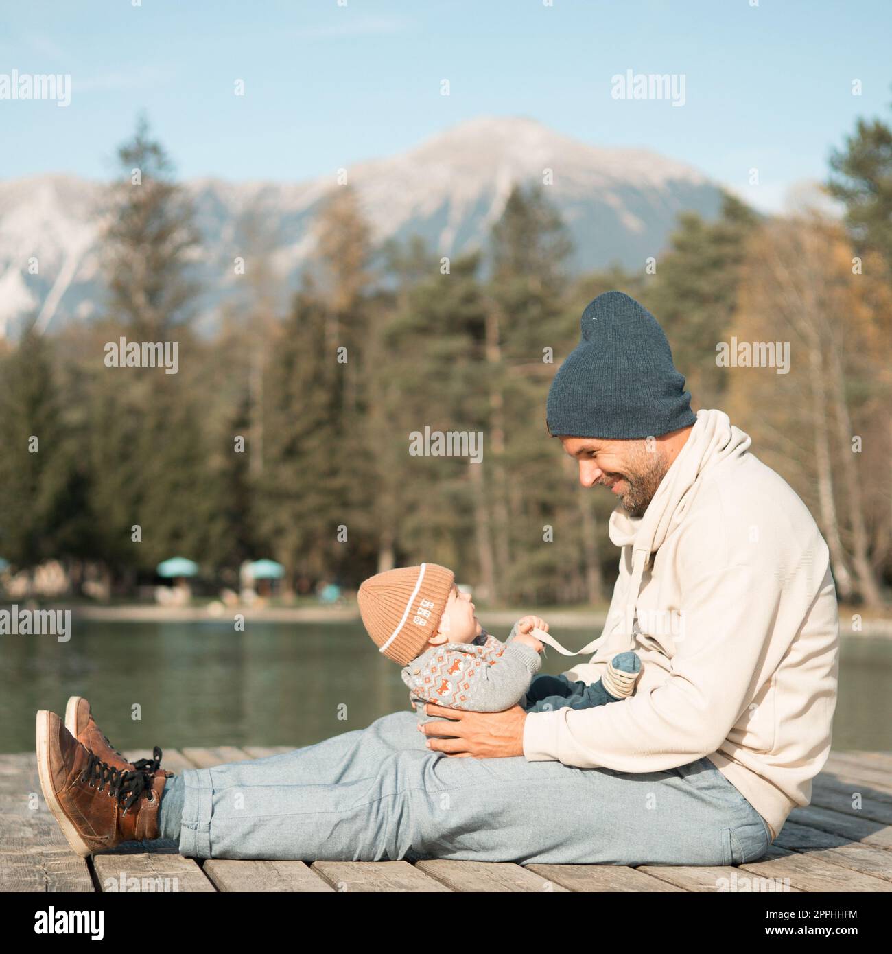 Glückliche Familie. Vater spielt mit ihrem kleinen Jungen an einem sonnigen Herbsttag außerhalb der Tür. Porträt von Vater und Sohn auf einer hölzernen Plattform am See. Positive menschliche Emotionen, Gefühle, Freude. Stockfoto