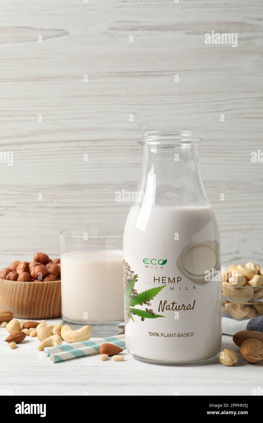 Glas und Flasche Hanfmilch und verschiedene Nüsse auf einem weißen Holztisch. Veganes Produkt Stockfoto