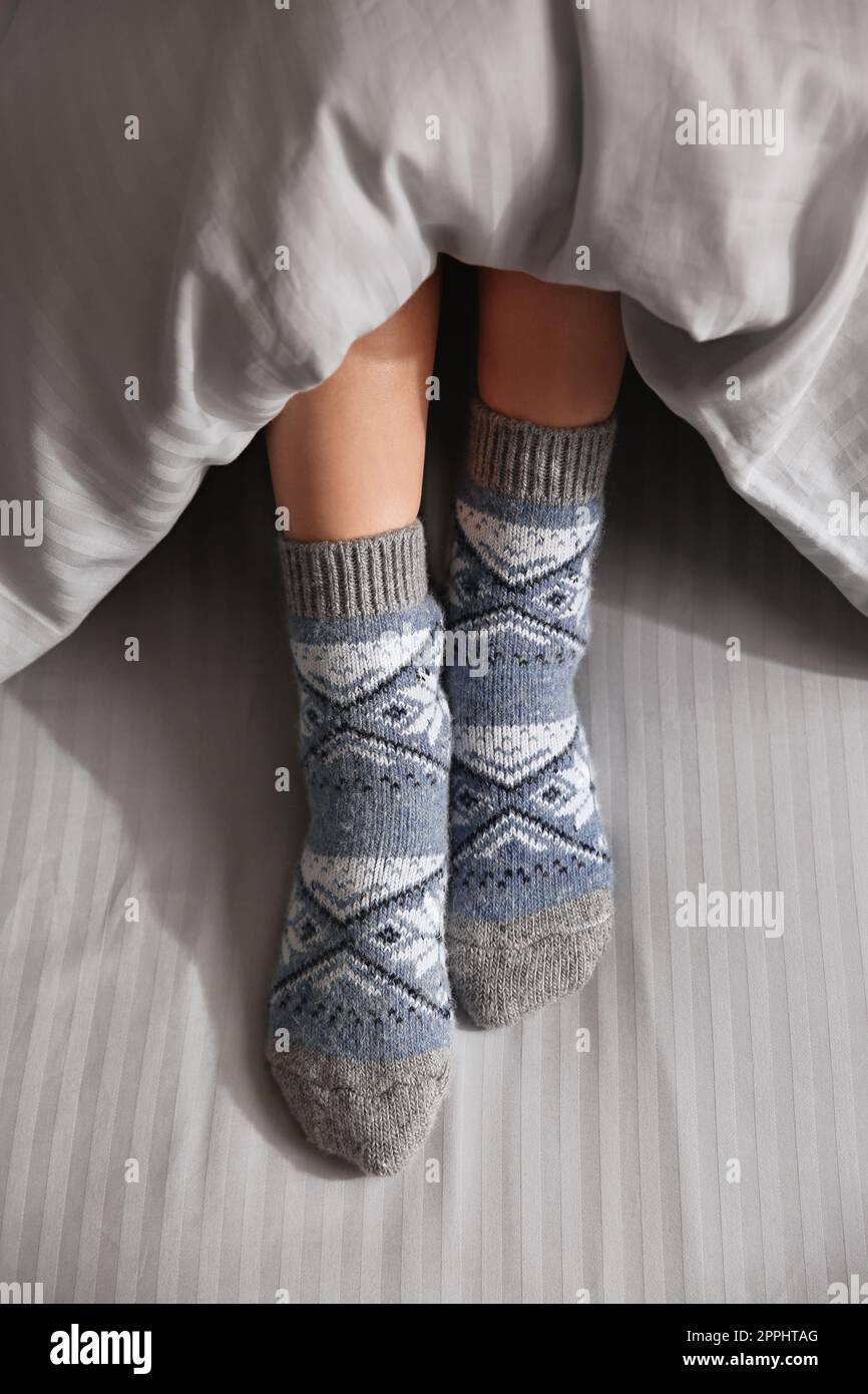 Eine Frau trägt gestrickte Socken unter einer Decke im Bett, Nahaufnahme Stockfoto