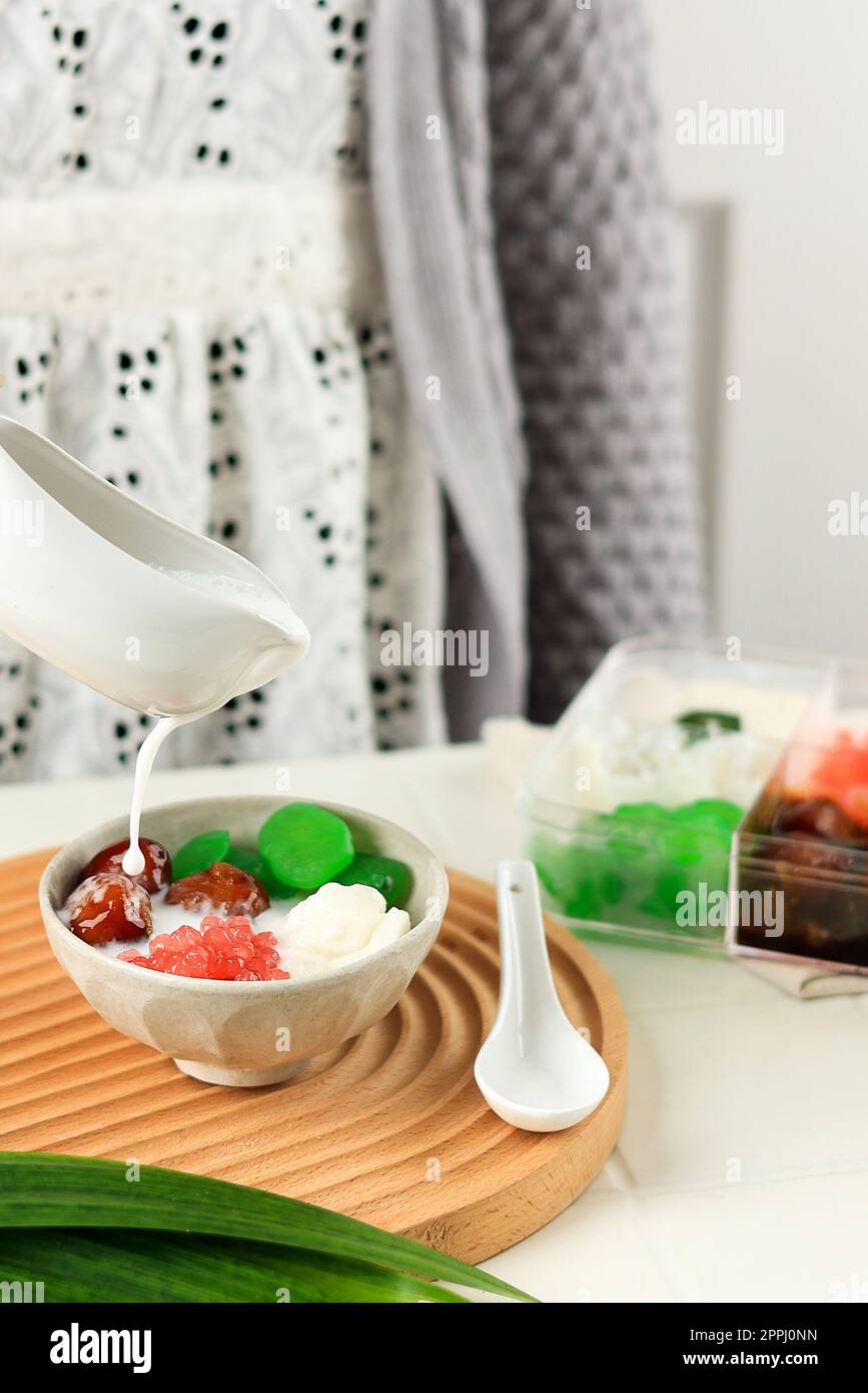 Gieße Kokosnusssoße in die Schüssel mit Kolak Campur oder süßem Mischporridge, beliebtes Dessert aus Indonesien Stockfoto