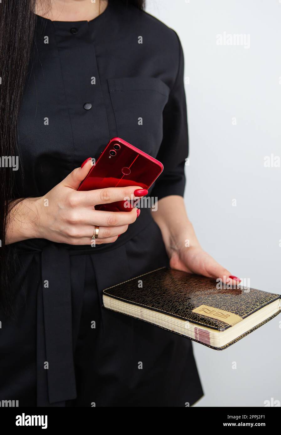 Eine Geschäftsfrau in schwarzer Uniform steht und hält ein Smartphone und ein Notizbuch über die Arbeit in ihrem Schönheitssalon. Konzept von Kleinunternehmen, Schönheitssalon und Selbstpflege. Stockfoto