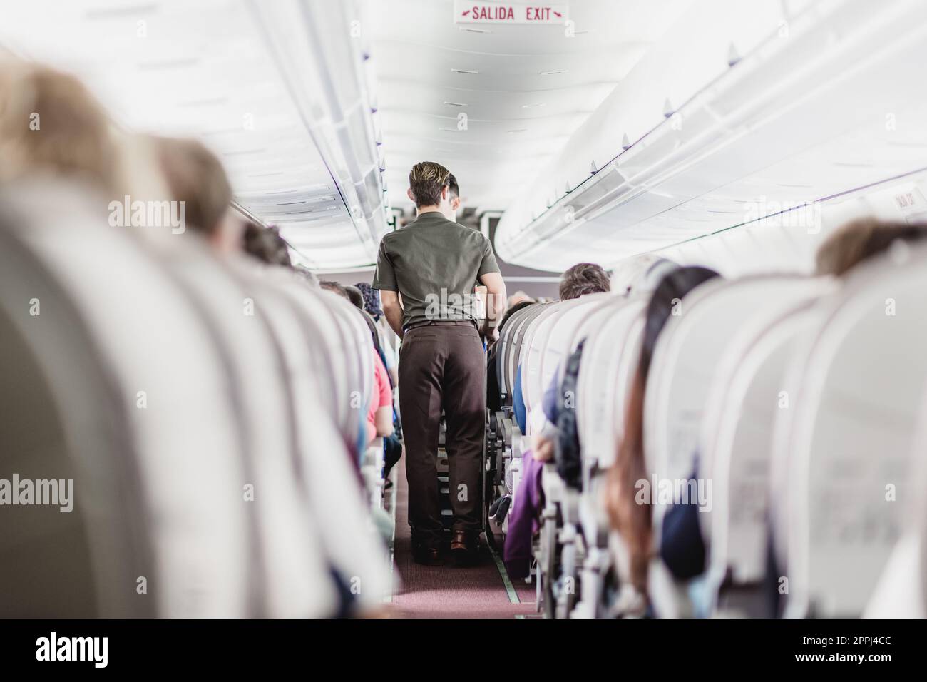 Flugzeuginnenraum mit Passagieren auf Sitzen und Steward, der durch den Gang geht Stockfoto