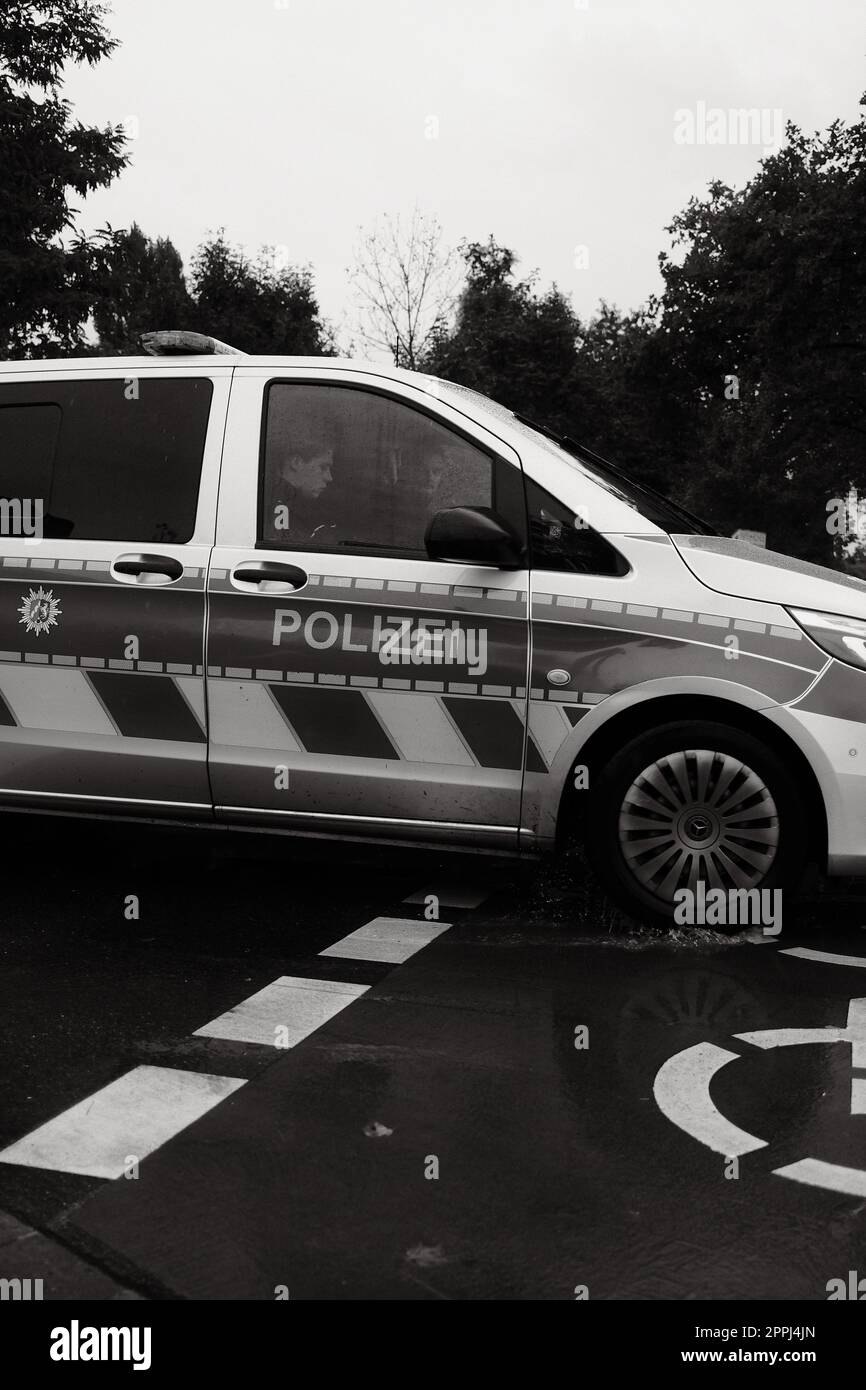 Vertikale Grauskala zweier Polizisten in einem deutschen Polizeiauto an einem Regentag in Düsseldorf Stockfoto