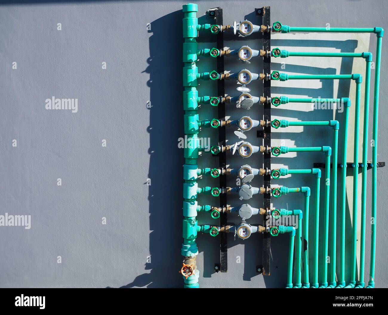 Wasserzählerplatten, Wasserarmaturen und grüne Wasserleitungen an der Gebäudewand Stockfoto