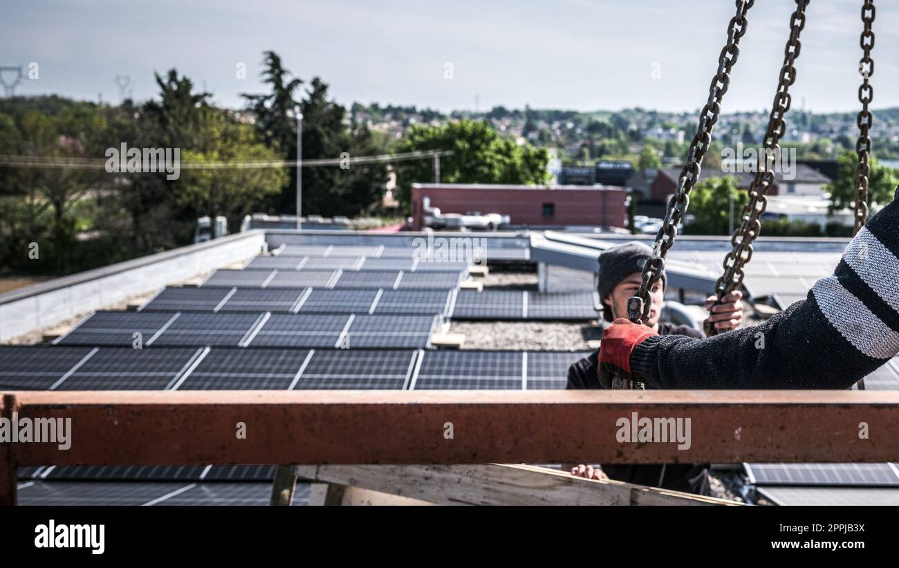 Männliche Teamingenieure, die eigenständige Solarpaneele installieren. Elektriker montieren blaues Solarmodul auf dem Dach des Unternehmens. Konzept alternativer Energien Stockfoto