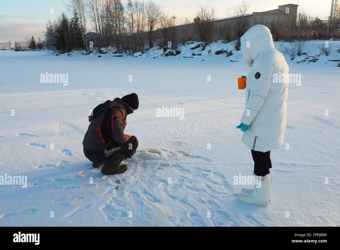 Logmozero, Karelien, Russland, 08. Januar 2022. Fischer und Fischer auf Winterfischerei. Ein Mann sitzt neben einem Loch in einem gefrorenen See und wartet auf einen Bissen. Schnee auf Eis, auf dem Boden nach Barsch fischen Stockfoto