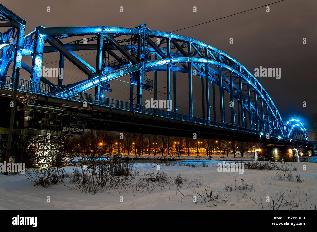 Blau beleuchtete Stahlbogenbrücke bei Nacht mit verschneitem Hintergrund Stockfoto